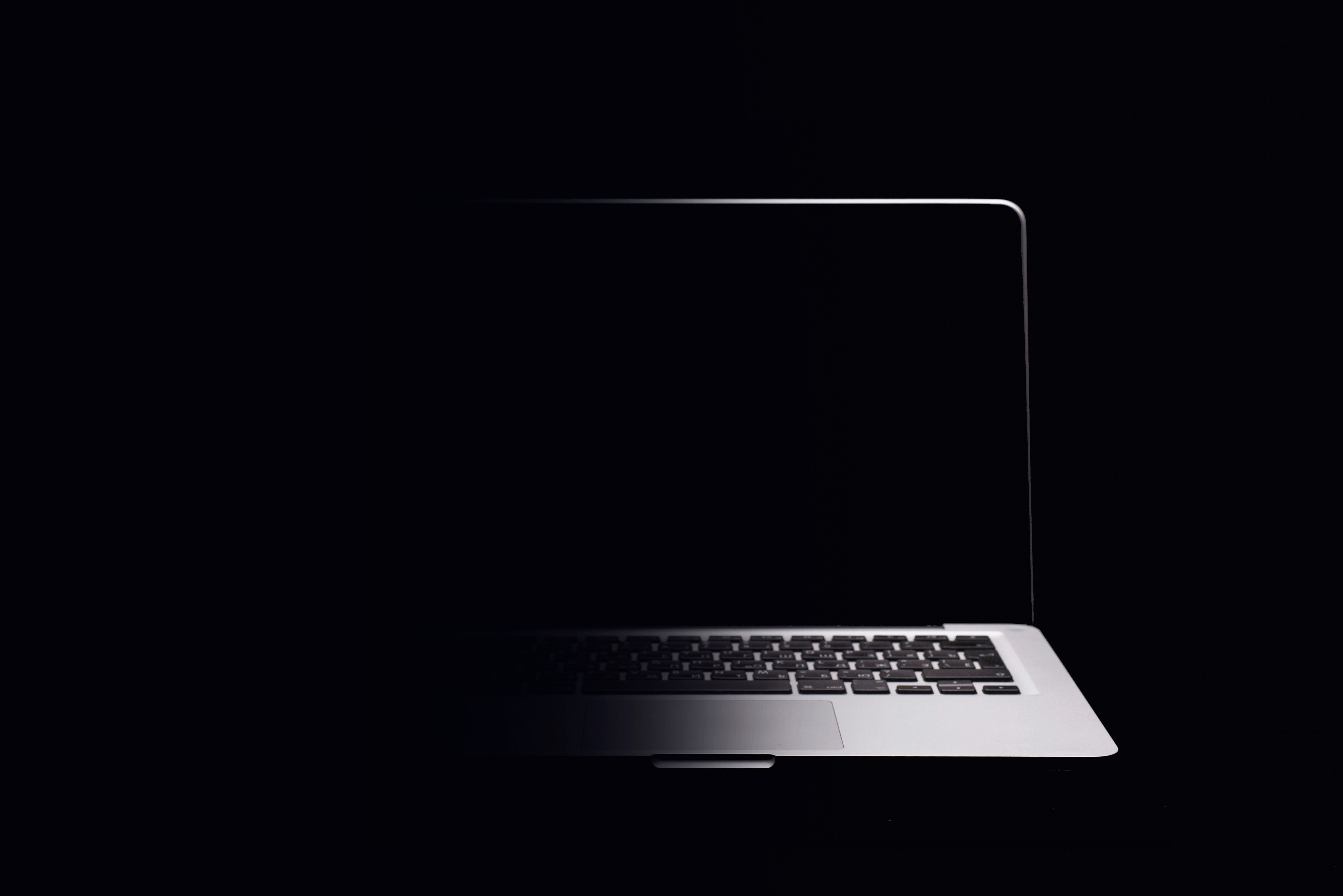 A silver laptop blending into the black background using a gradient of black to transparent from the left.